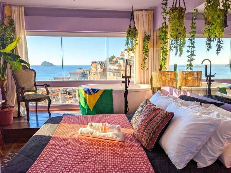 The bed faces a window over the houses of Vidigal and the sea, with the soaking tub beside it