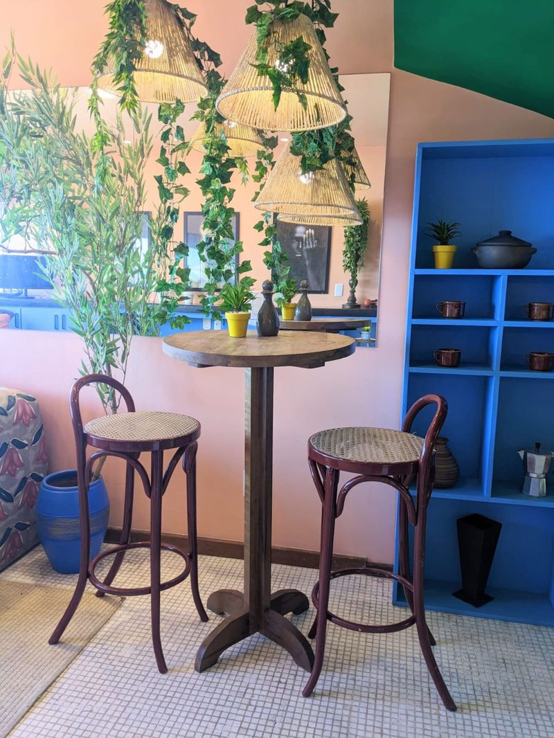 A round high table with two stools, blue shelves and hanging plants