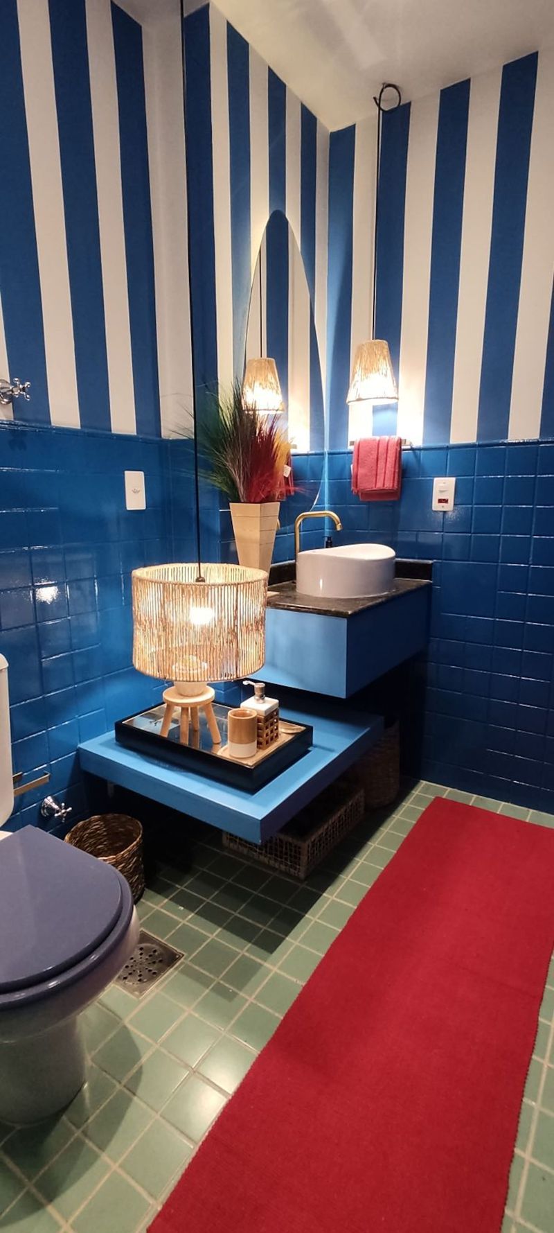 Blue tiles, a striped wall and a red rug in the bathroom
