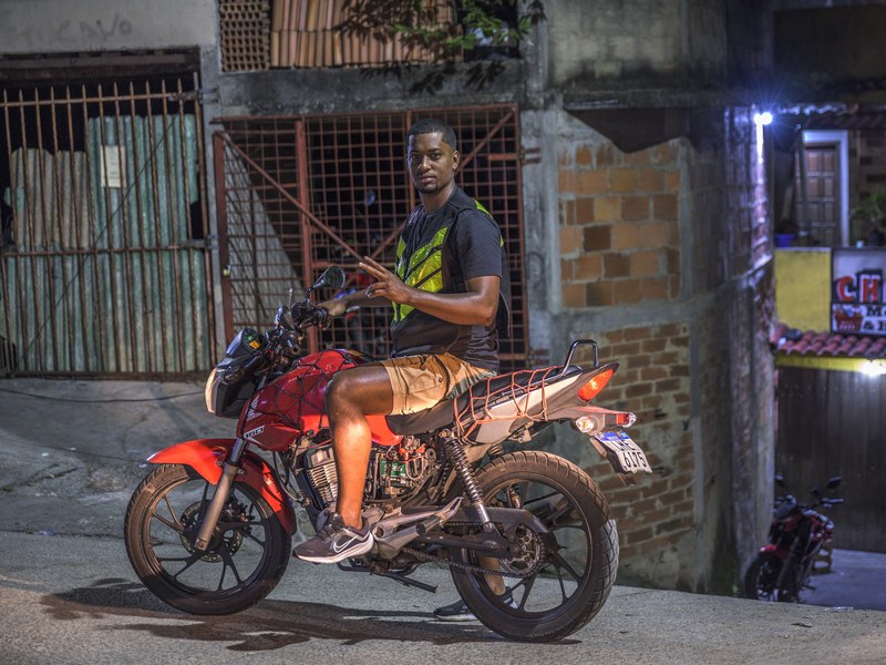 A man on a red motorbike on a street in Vidigal