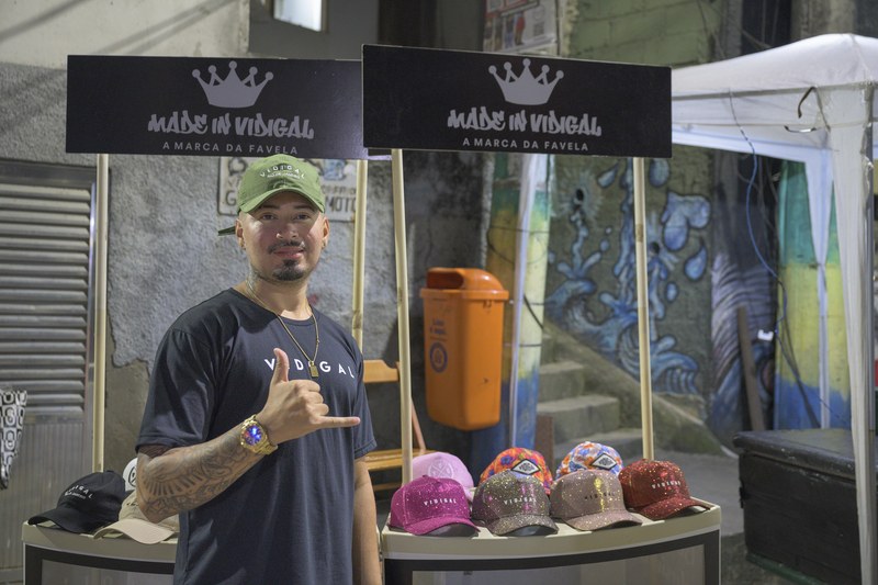 A vendor at a stall with a Made in Vidigal sign and caps for sale